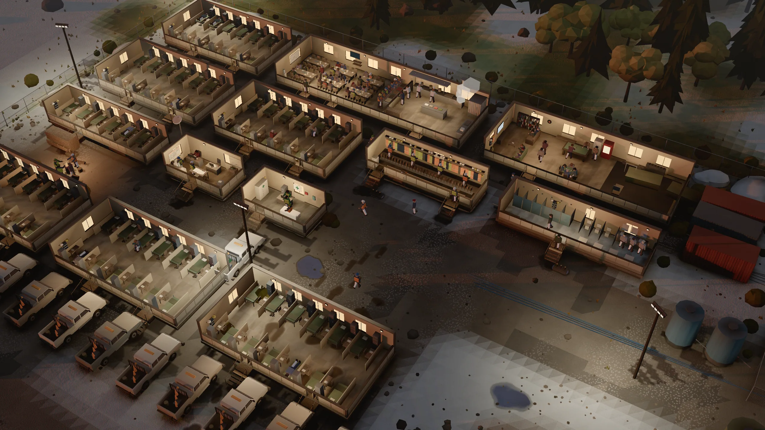 A work camp at evening: bunk houses, lit windows, trucks in the lot.